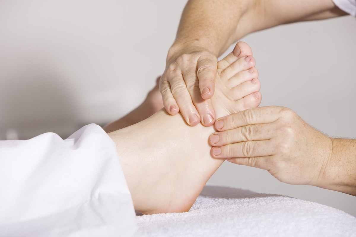 Un praticien masse le pied d'une cliente allongée sur une serviette