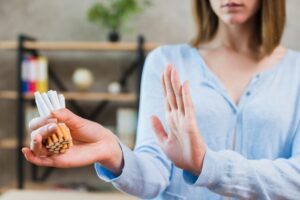 Femme faisant un geste de refus de la main devant un paquet de cigarettes écrasé — Arrêt du tabac : pourquoi le matériel choisi pèse autant que la motivation.