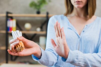 Femme faisant un geste de refus de la main devant un paquet de cigarettes écrasé — Arrêt du tabac : pourquoi le matériel choisi pèse autant que la motivation.