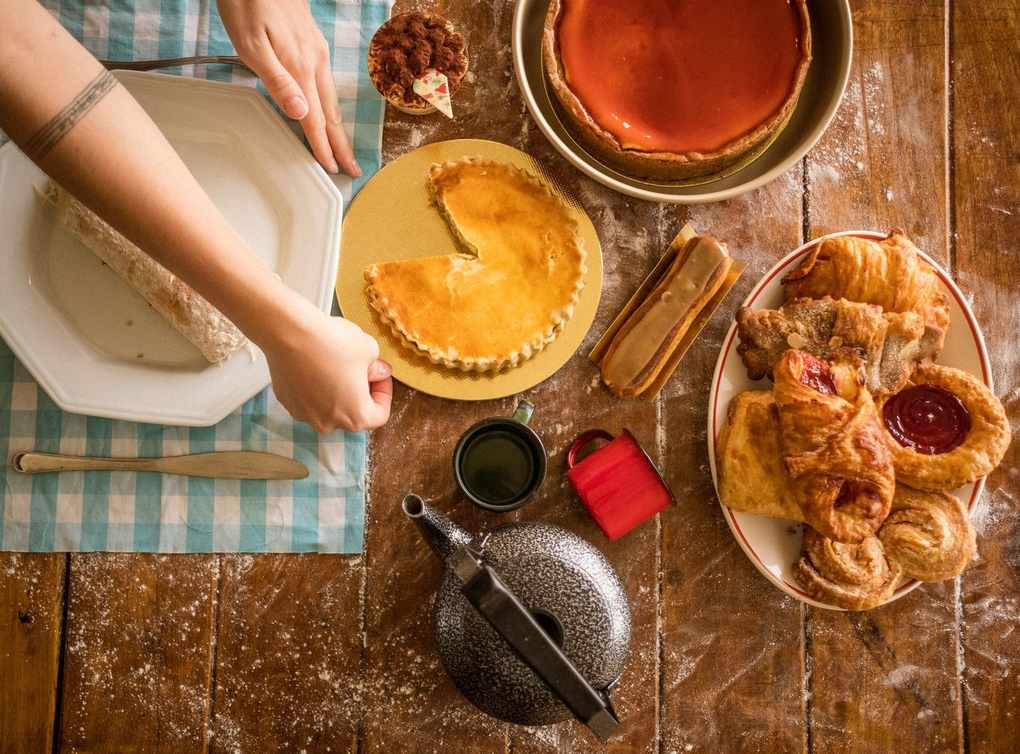 Main plaçant un plat sur une table en bois avec desserts et ustensiles