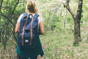 Une femme porte un sac à dos bleu et avance dans une forêt
