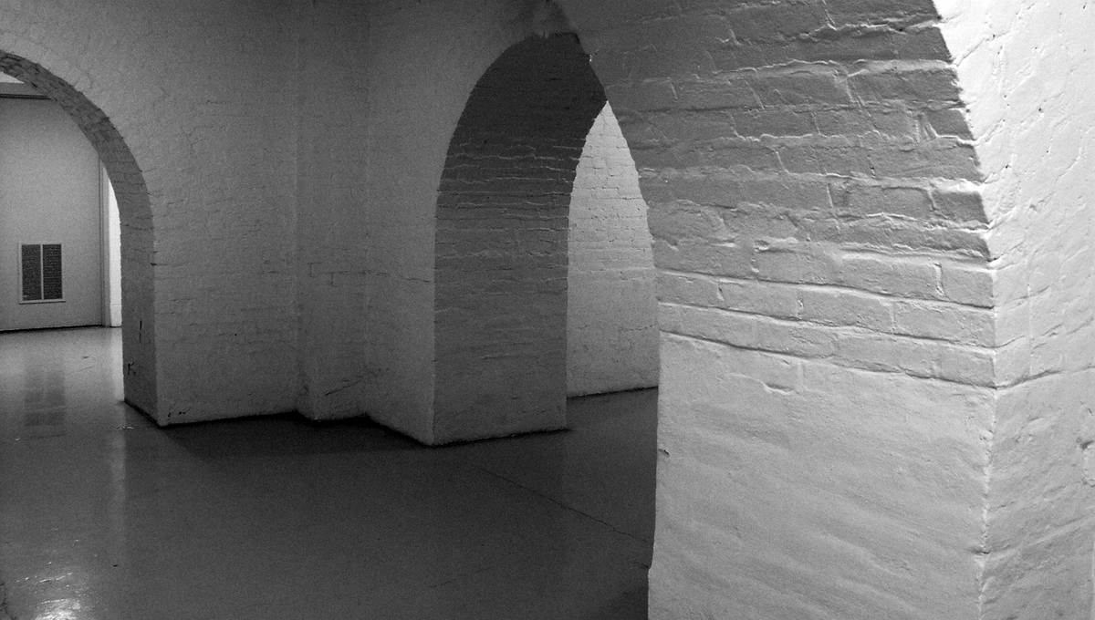 Corridor avec arches en briques blanches, sol brillant, portes et fenêtres visibles